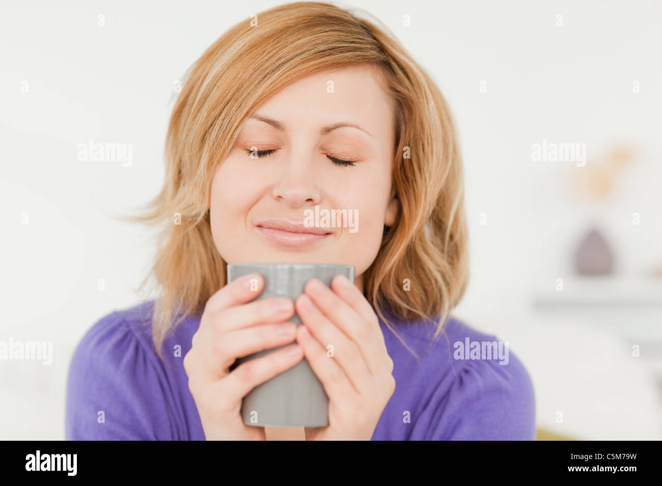 Prety i capelli rossi donna holding e annusare una tazza di caffè mentre è seduto su un divano Foto Stock