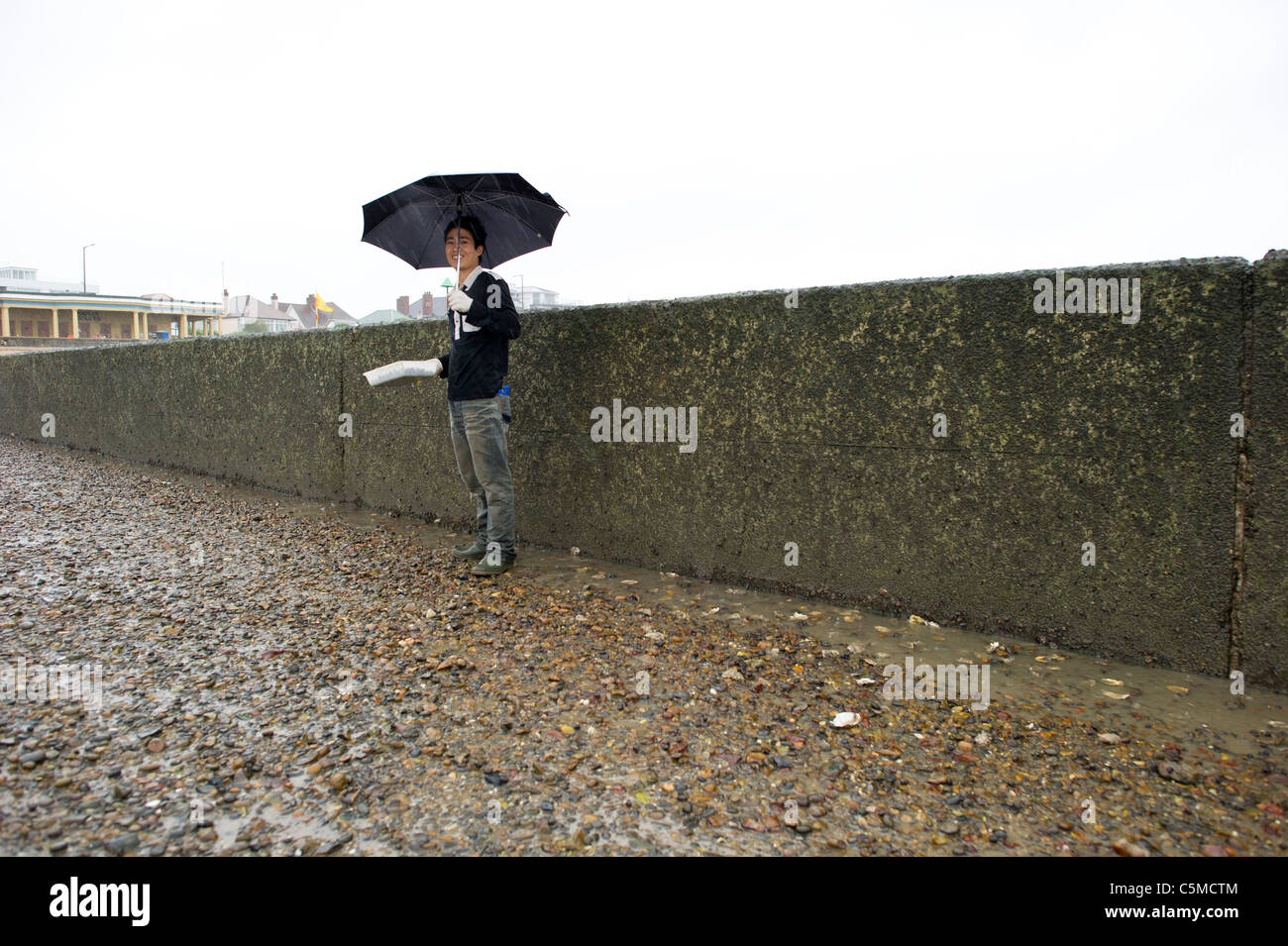 Un giovane cinese permanente maschio da un calcestruzzo groyne a Southend on Sea mostrando i lupini ha raccolto durante la bassa marea. Foto Stock