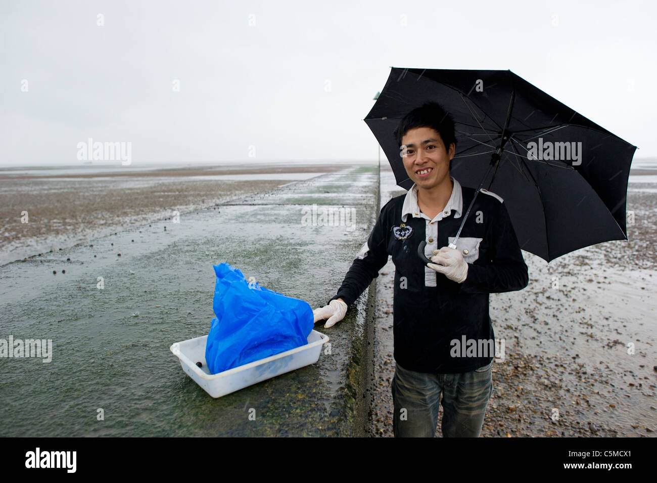 Un giovane cinese permanente maschio da un calcestruzzo groyne a Southend on Sea mostrando i lupini ha raccolto durante la bassa marea. Foto Stock