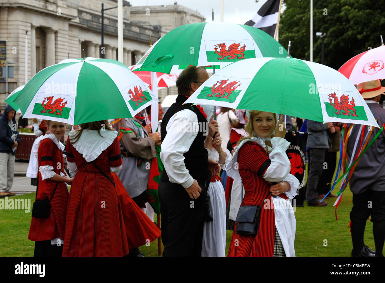 Ballerini in abito tradizionale riparo sotto gli ombrelloni sul giorno Midsummers, Cathays Park, Cardiff, South Glamorgan, Wales, Regno Unito Foto Stock