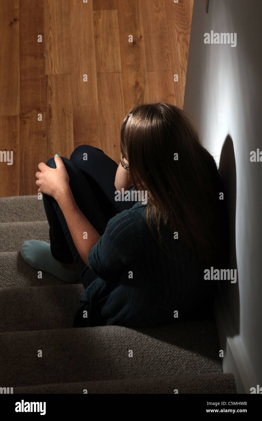 Giovane donna bionda seduto da solo al buio, mano sulla testa, vista posteriore. Foto Stock