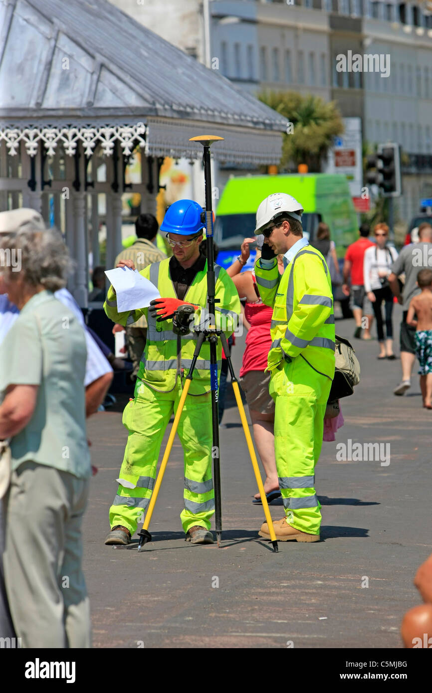 Due uomini vestiti in Dayglo tute giallo geo-mapping Weymouth waterfront nel Dorset Foto Stock