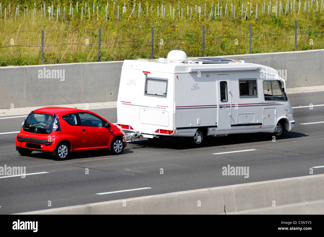 Laterale e posteriore del bianco francese Le Voyageur LVX camper rosso di traino Citreon C1 auto percorrendo l autostrada del Regno Unito per un stile di vita in viaggio Foto Stock