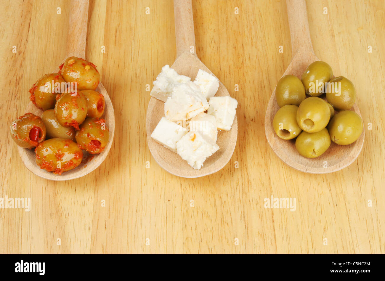 Olive e formaggio feta in cucchiai di legno su una tavola di legno Foto Stock