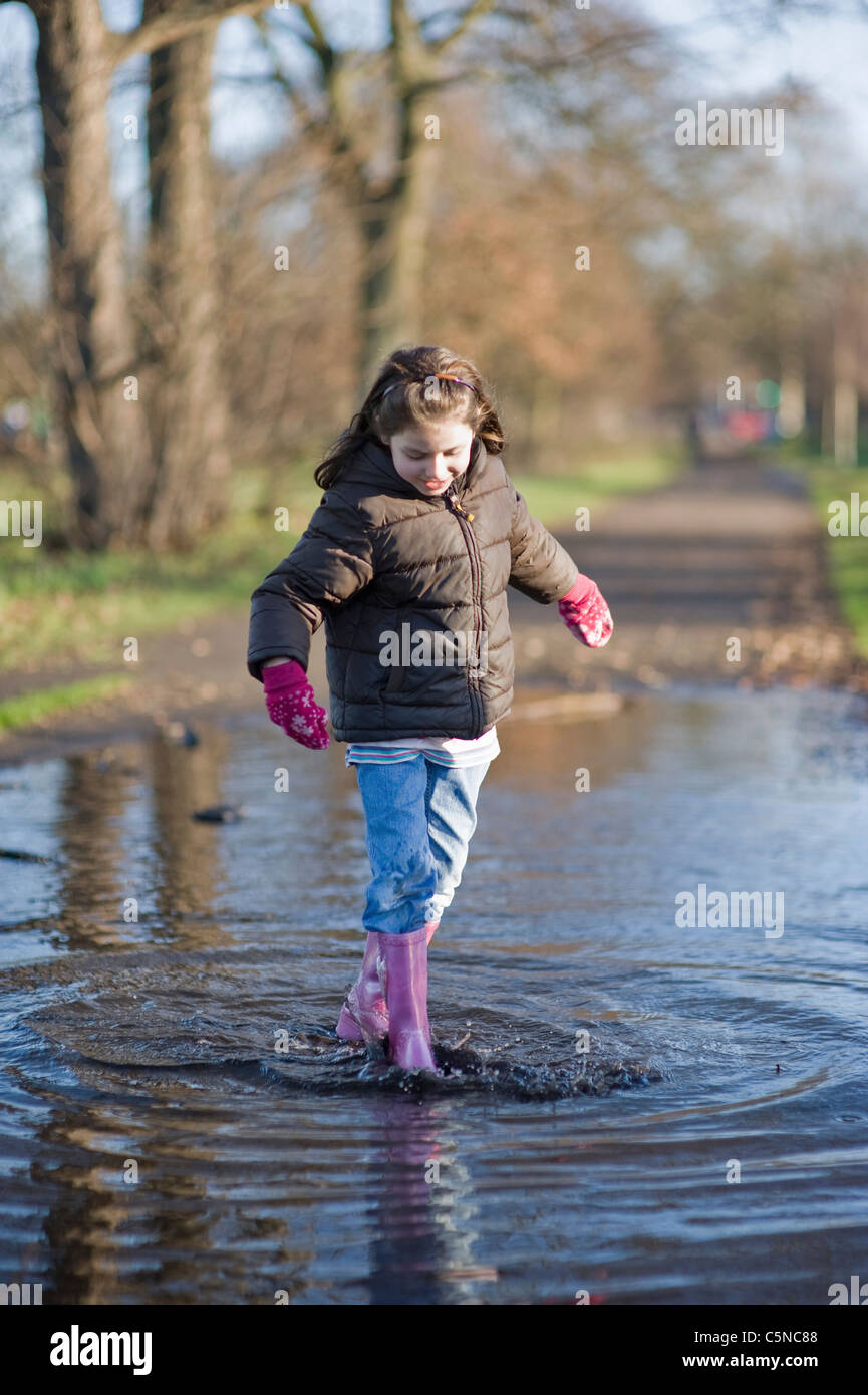 Una giovane ragazza camminare attraverso una pozzanghera, sorridente Foto Stock