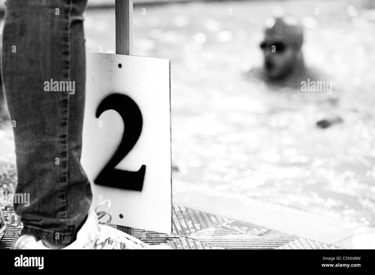 Un funzionario può contenere un giro a bordo del contatore dal bordo della piscina durante un triathlon nuoto evento. In bianco e nero. Foto Stock