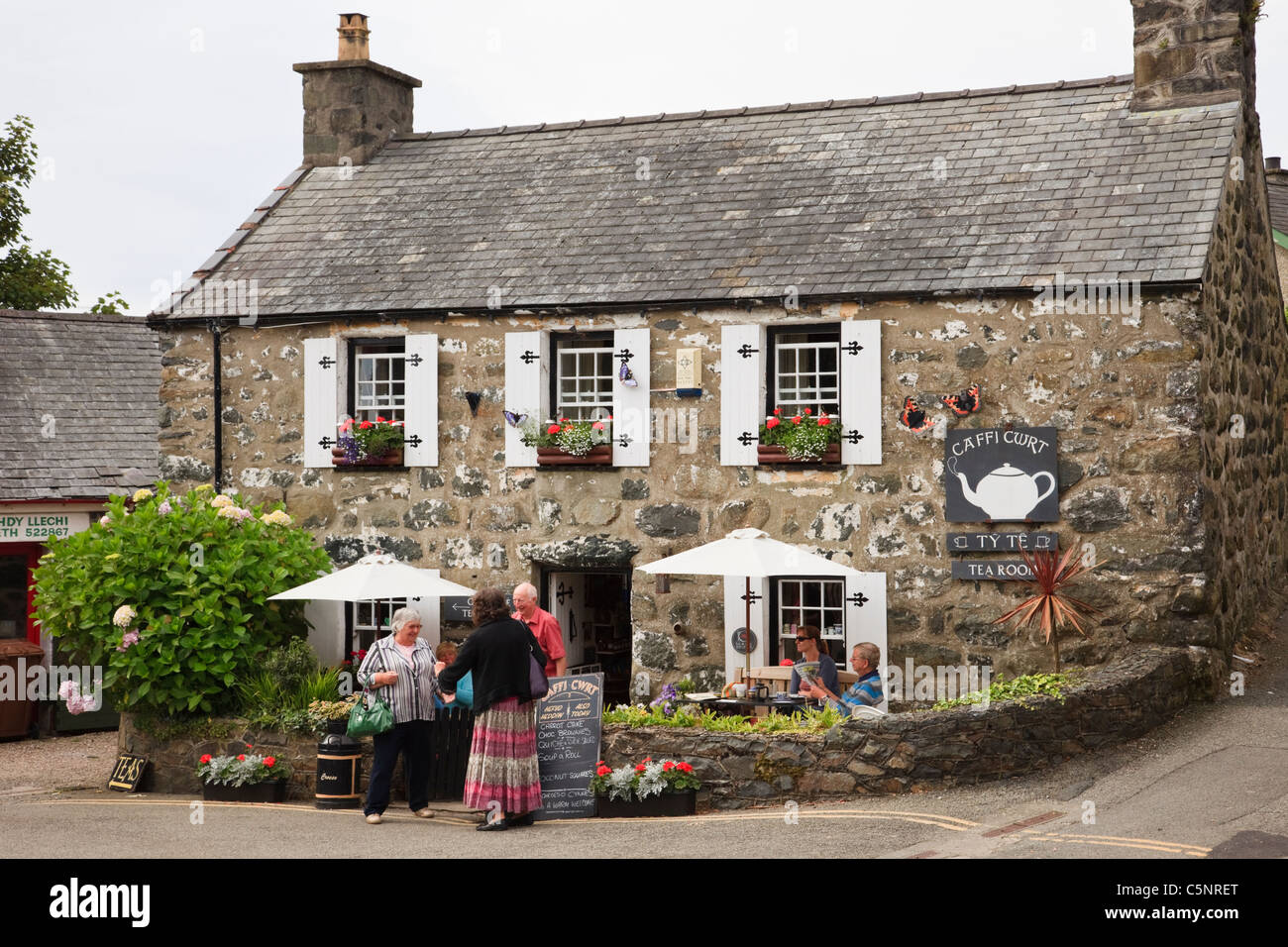 Sale da tè in un tradizionale cottage in pietra con persone sedute all'esterno. Criccieth, Lleyn Peninsula, Gwynedd, Galles del Nord, Regno Unito. Foto Stock