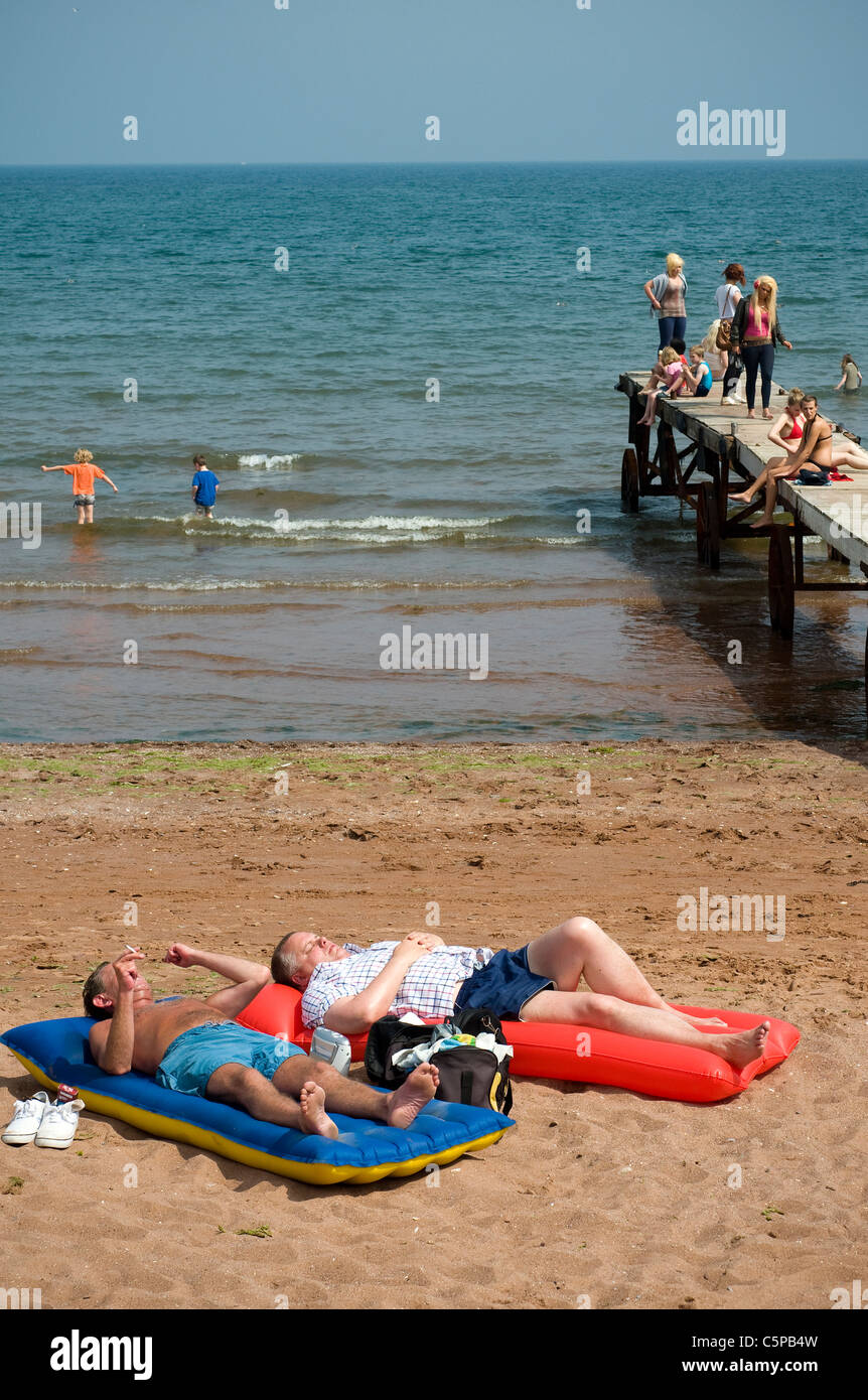 Staycation Gran Bretagna gode di mini-ondata di caldo,uomini di mezza età su materassini gonfiabili a Paignton Beach ha infranto record come temperature soar Foto Stock