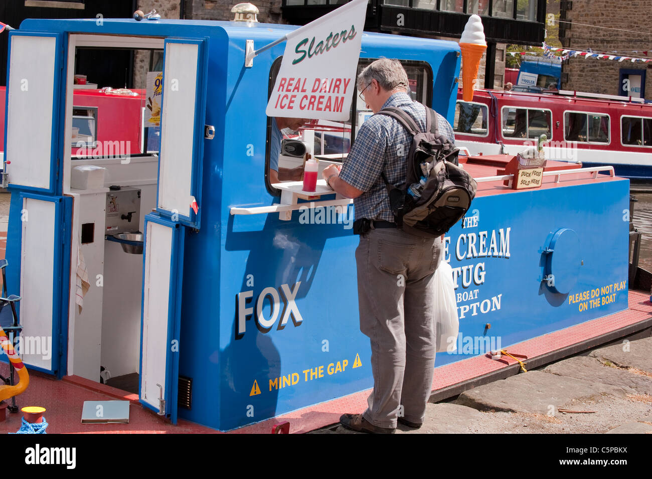 1 uomo che serve e vende gelati a un cliente maschile in piedi al banco di una barca da rimorchiatore convertita 'Fox' - Leeds Liverpool Canal, Skipton, Yorkshire, GB, UK Foto Stock