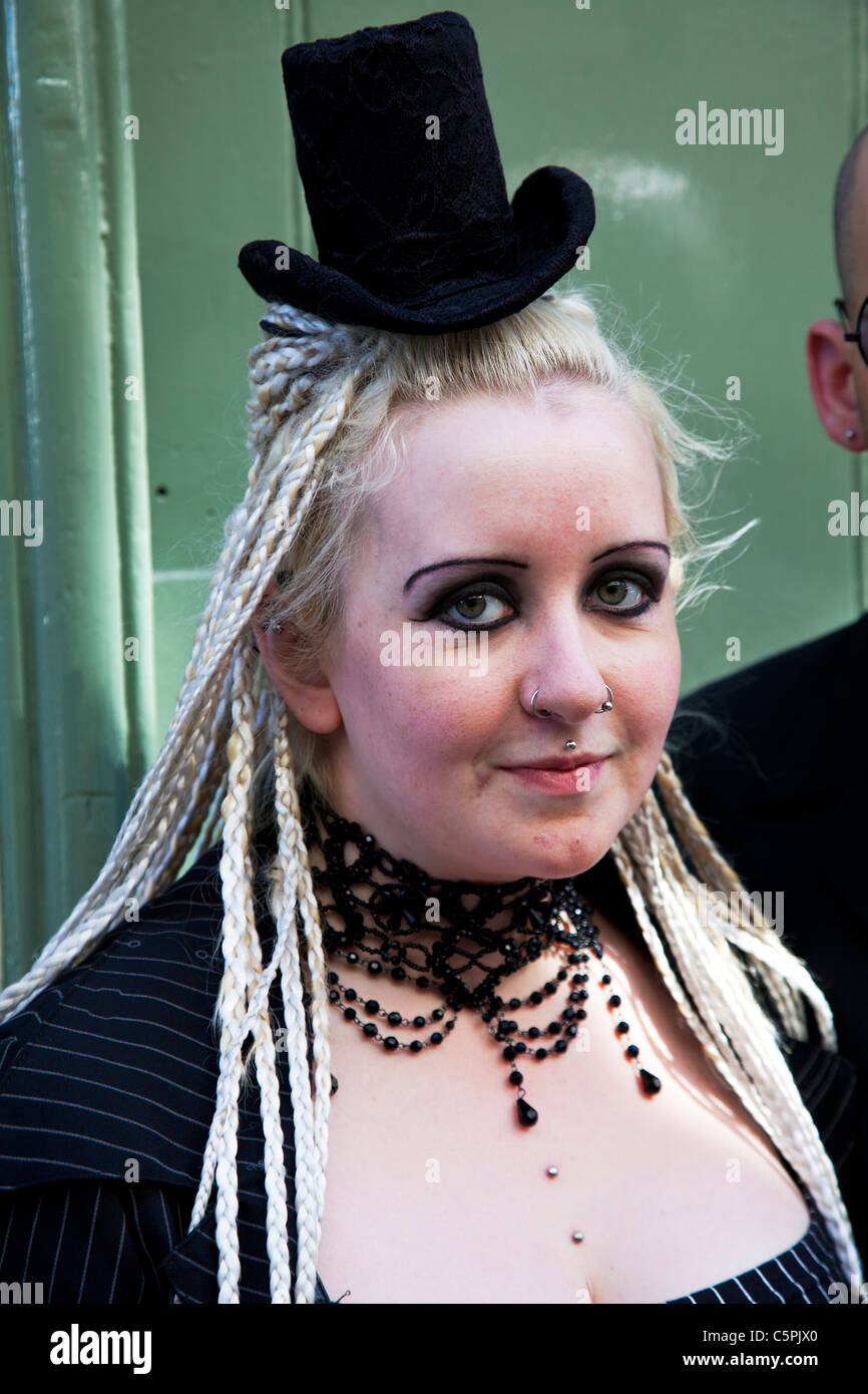 Whitby, nello Yorkshire, Inghilterra, goth donna con piercing nel naso e il labbro con hat troppo piccolo per la sua testa, biondo dreadlocks Foto Stock