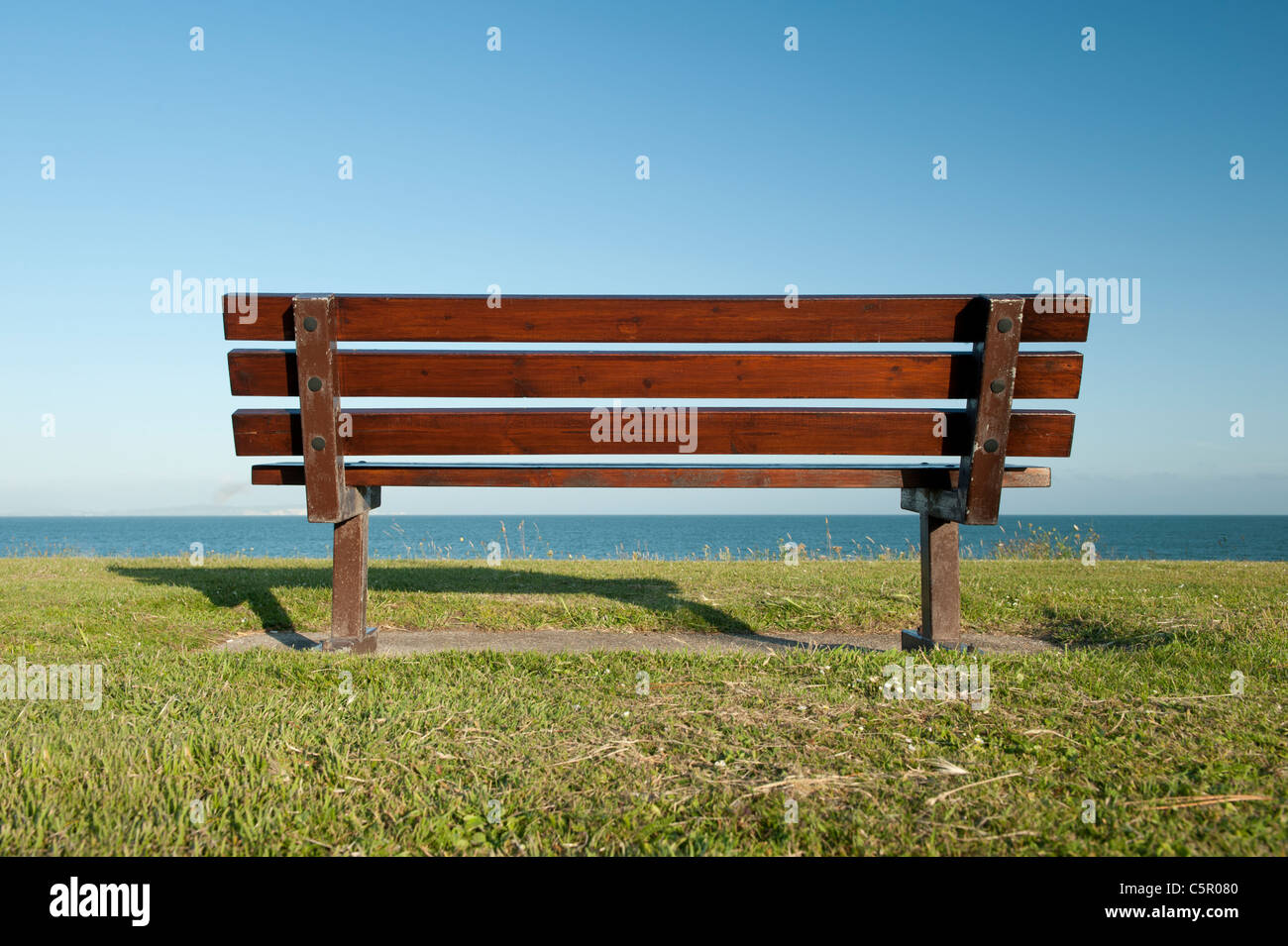 Un vuoto banco pubblico rimane non occupato si affaccia su un tranquillo e ancora mare a Mudeford, Dorset. Foto Stock