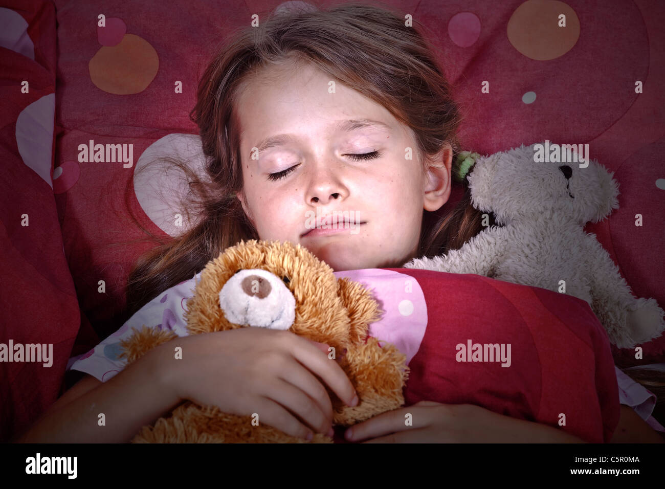 Un otto-anno-vecchia ragazza nel letto con coperte e cuscini e animali impagliati Foto Stock