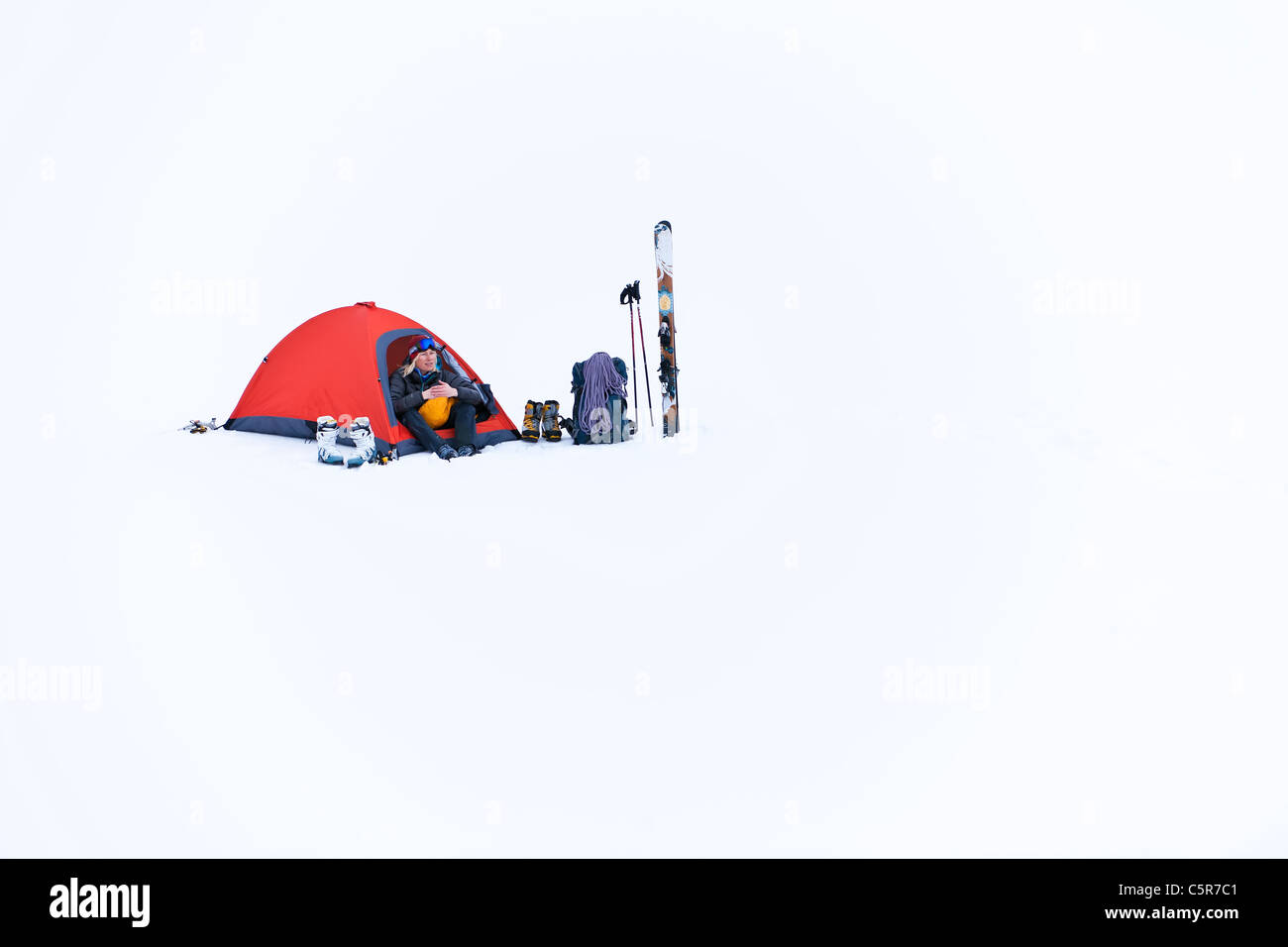 Una donna cercando di tenere in caldo seduto nella sua tenda sulla Montagna neve. Foto Stock