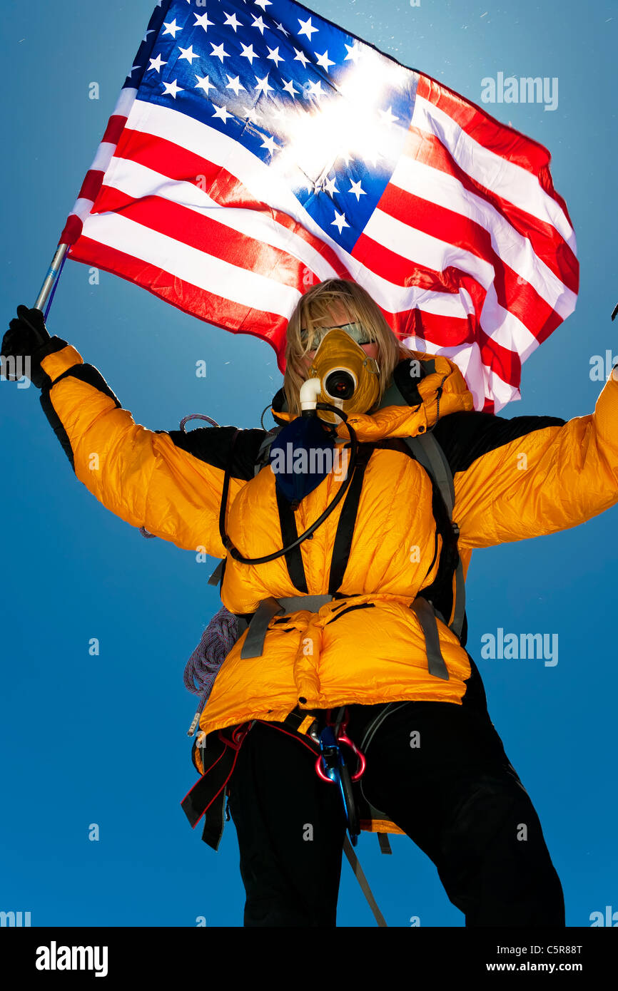 Un alpinista con autorespiratore ad ossigeno celebra e onde la bandiera statunitense dopo il raggiungimento del vertice. Foto Stock