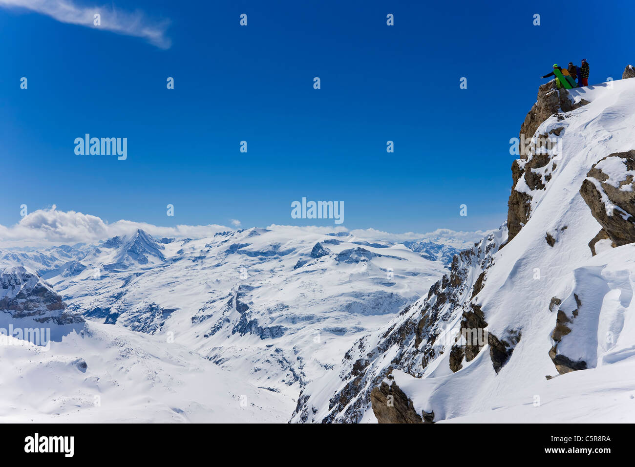 Tre gli snowboarder in piedi su una montagna innevata guardare oltre le cime e picchi di seguito. Foto Stock