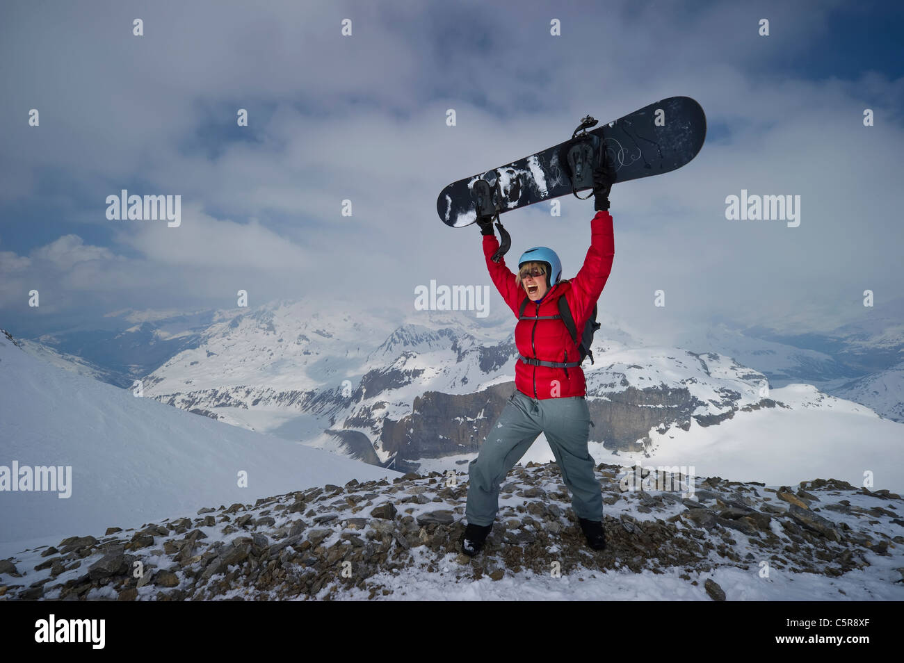 Uno snowboarder celebra essendo sulla sommità delle montagne coperte di neve. Foto Stock