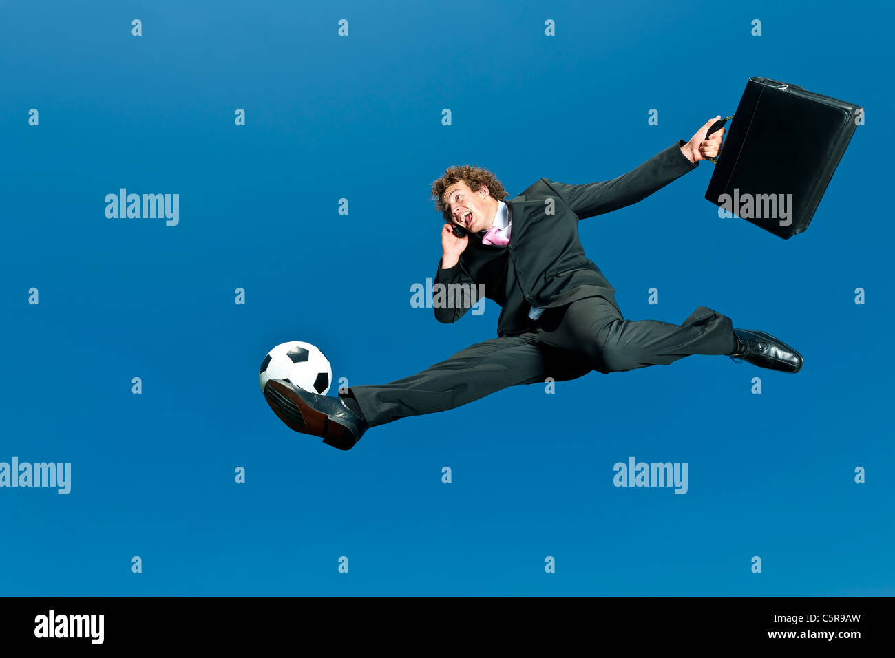 Un calcio giocando imprenditore volleys palla mentre sul cellulare. Foto Stock