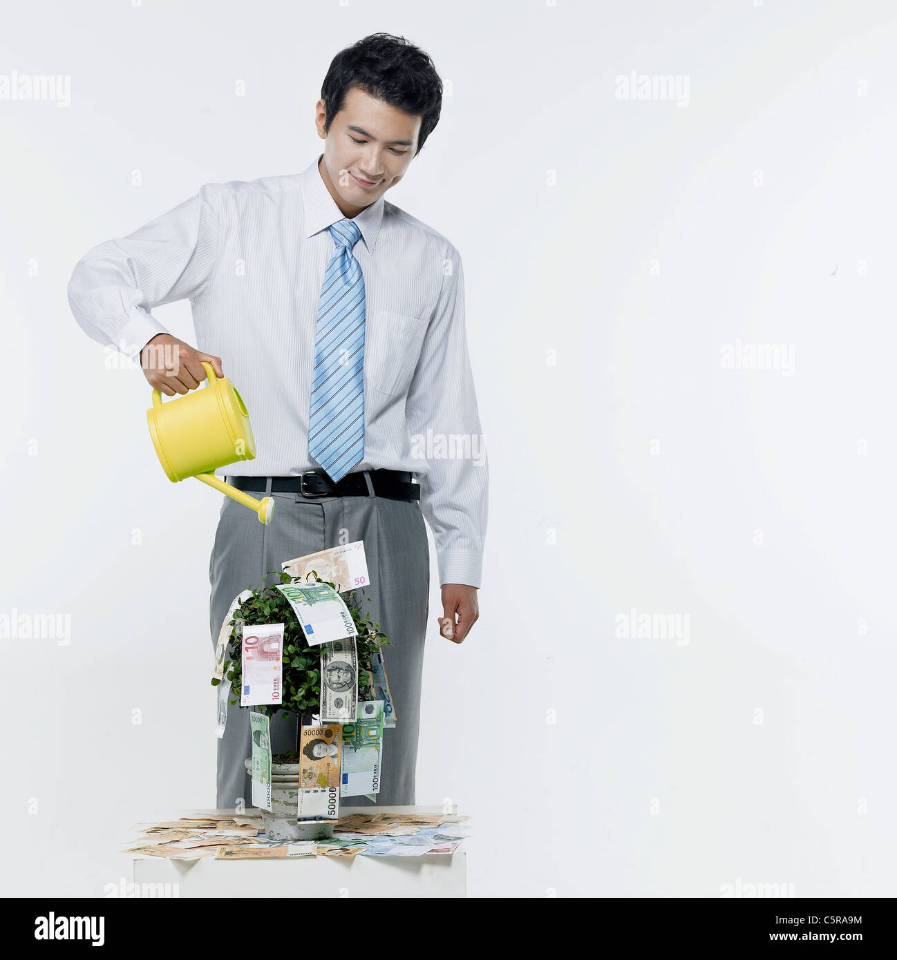Un uomo di irrigazione di un vaso di fiori pieno di carta moneta Foto Stock