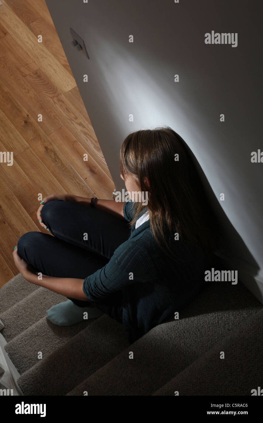 Giovane ragazza seduta sulle scale scuro vista posteriore Foto Stock