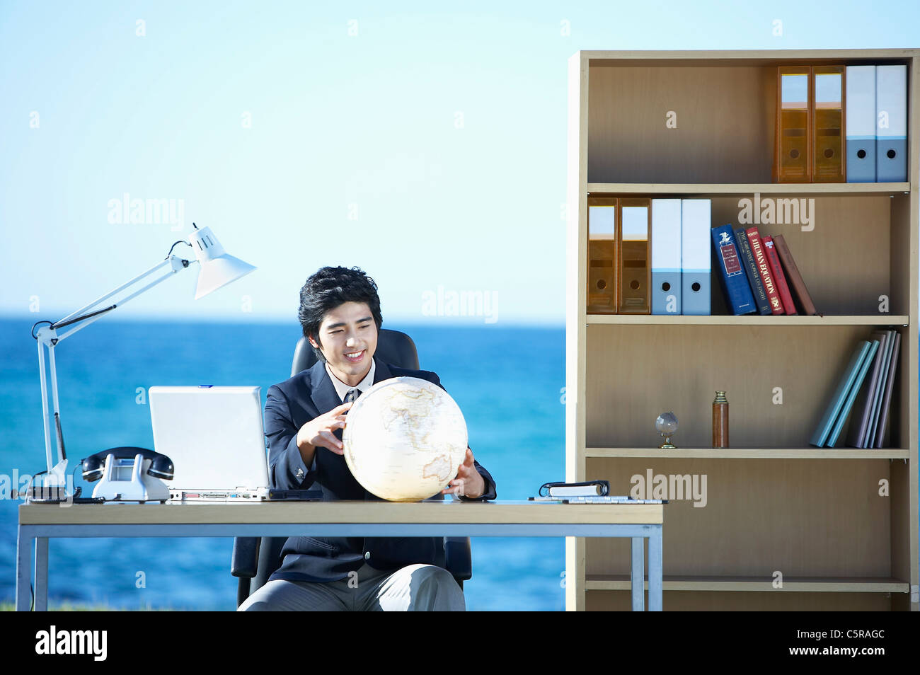 Un uomo holding globe seduto alla sua scrivania in ufficio al di fuori Foto Stock