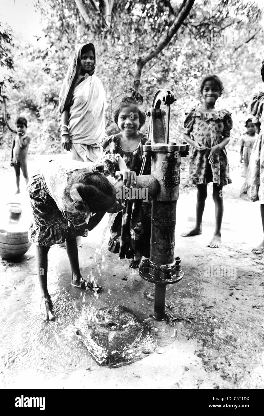 I bambini giocano spensierati e bere acqua da una pompa di acqua nei borghi collinari di Orissa in India . Progetto di Oxfam Foto Stock