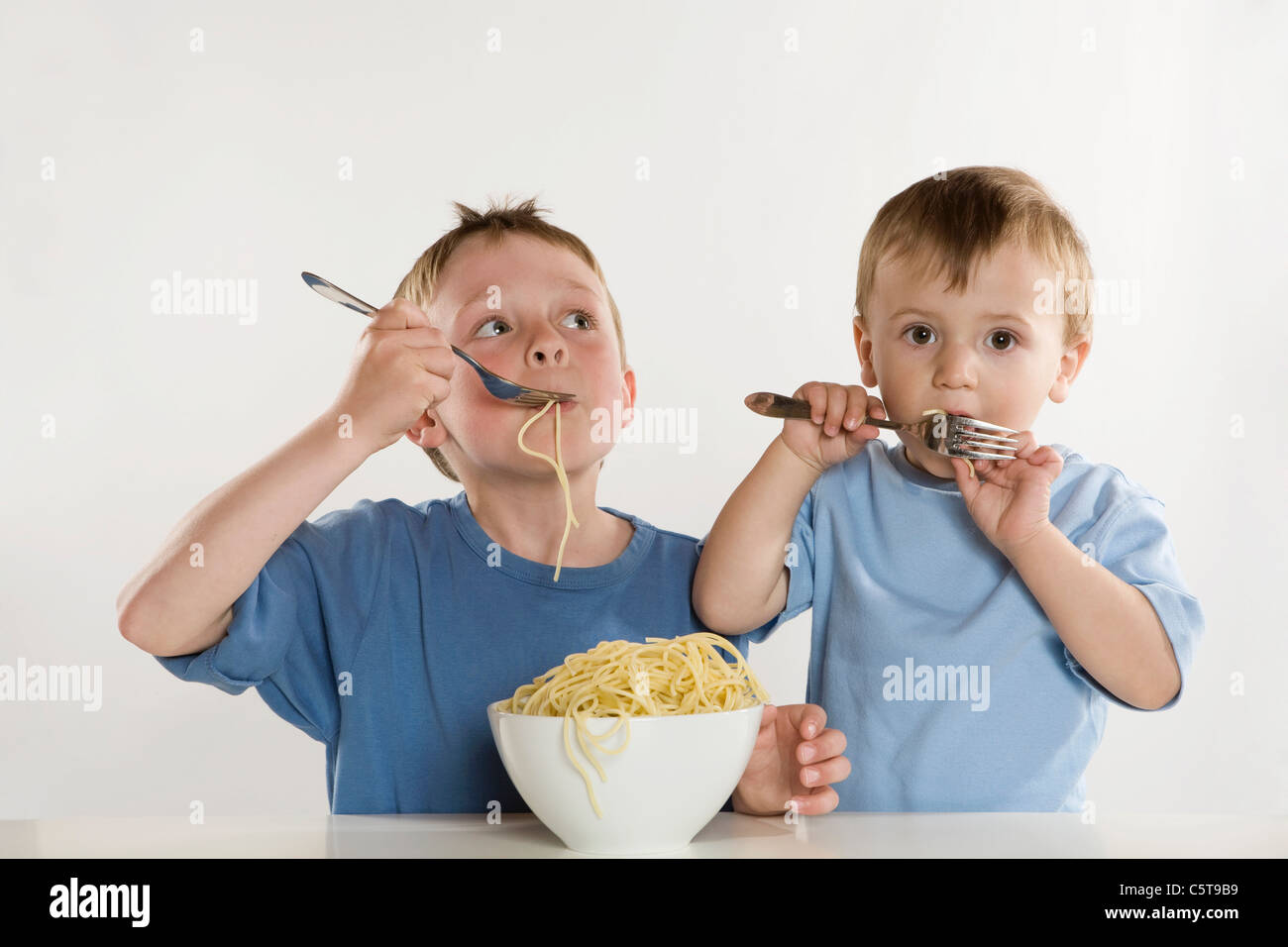 Due ragazzi (6-7) (2-3) Mangiare spaghetti, ritratto Foto Stock