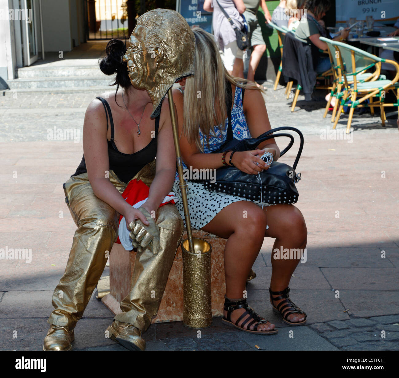 Il golden statico di figura su Stroeget a Copenaghen è una ragazza - ora rilassante all'ombra con un amico dietro la maschera dorata Foto Stock