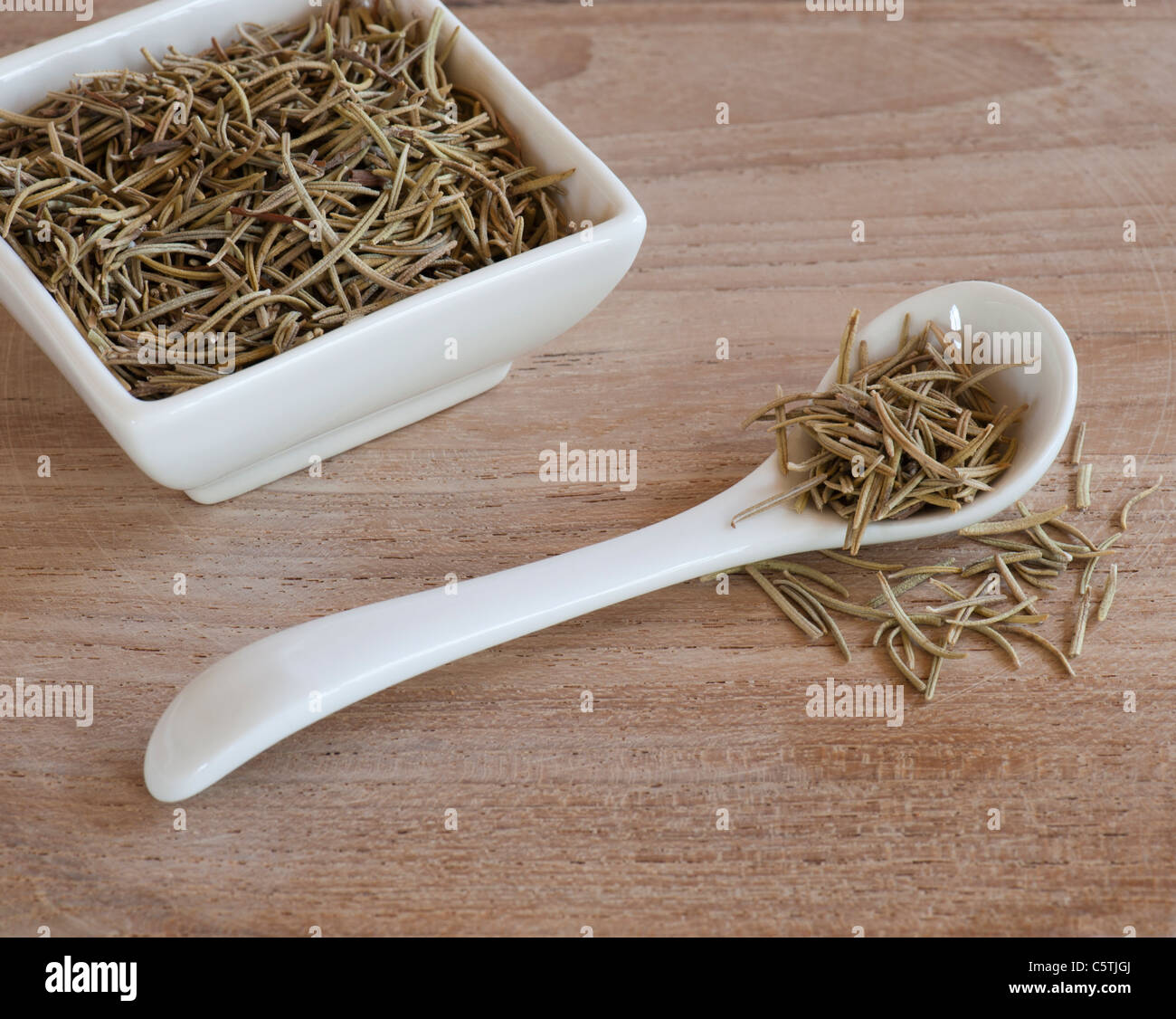Un cucchiaio e Dishful di Aromatiche foglie di rosmarino, su una tavola di legno sulla superficie di lavoro Foto Stock