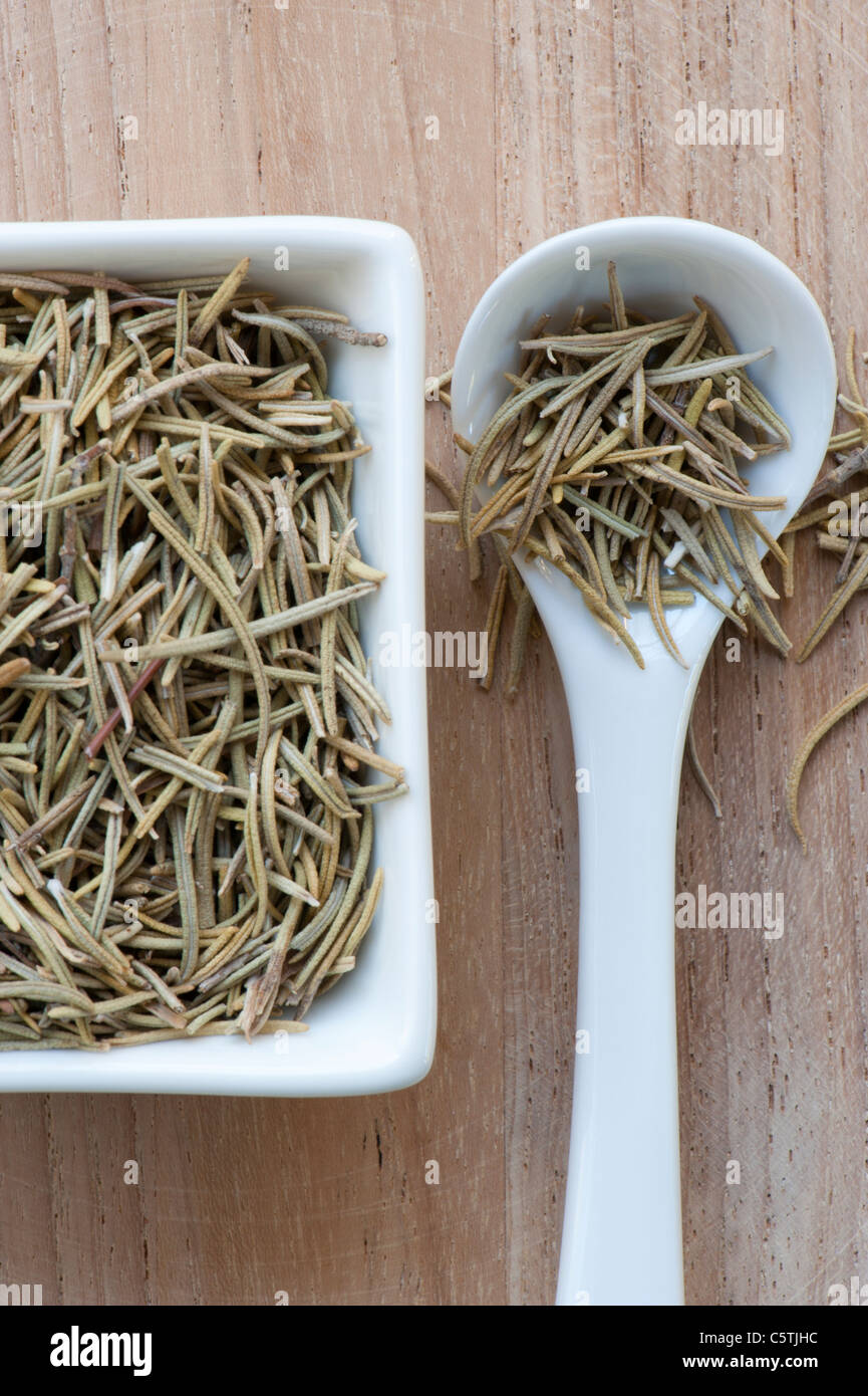 Rosmarino essiccato In piatto con il cucchiaio, prevista su una superficie in legno Foto Stock
