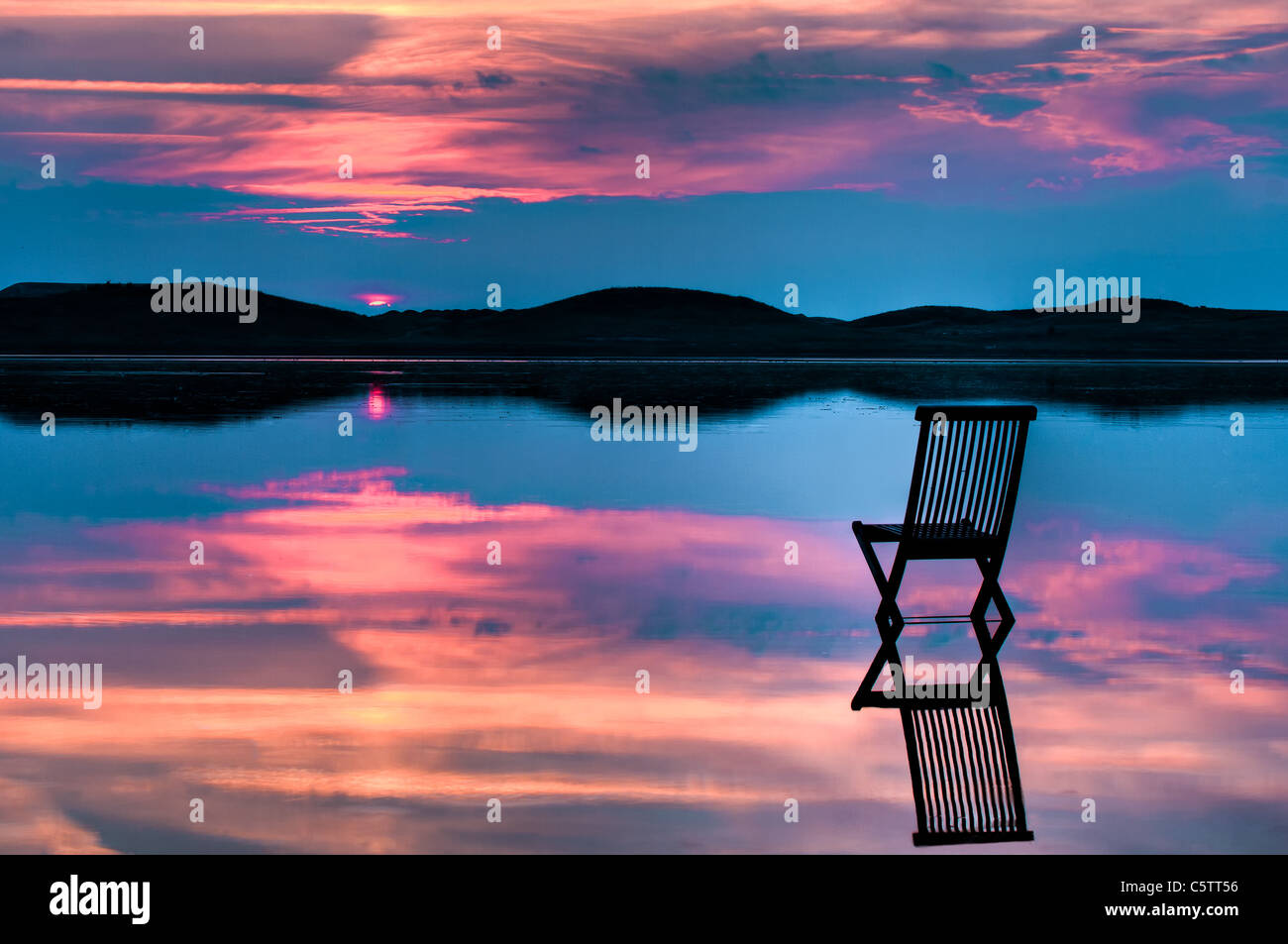 Vista panoramica del tramonto su ingresso e colline con una sedia in acque calme, con riflessi del tramonto e sedia. Foto Stock