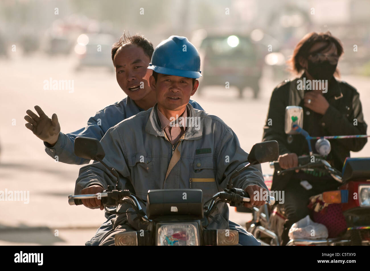 I lavoratori pendolari a lavorare sulla moto verso il basso strada polverosa, Dulan, Provincia di Qinghai, Cina Foto Stock