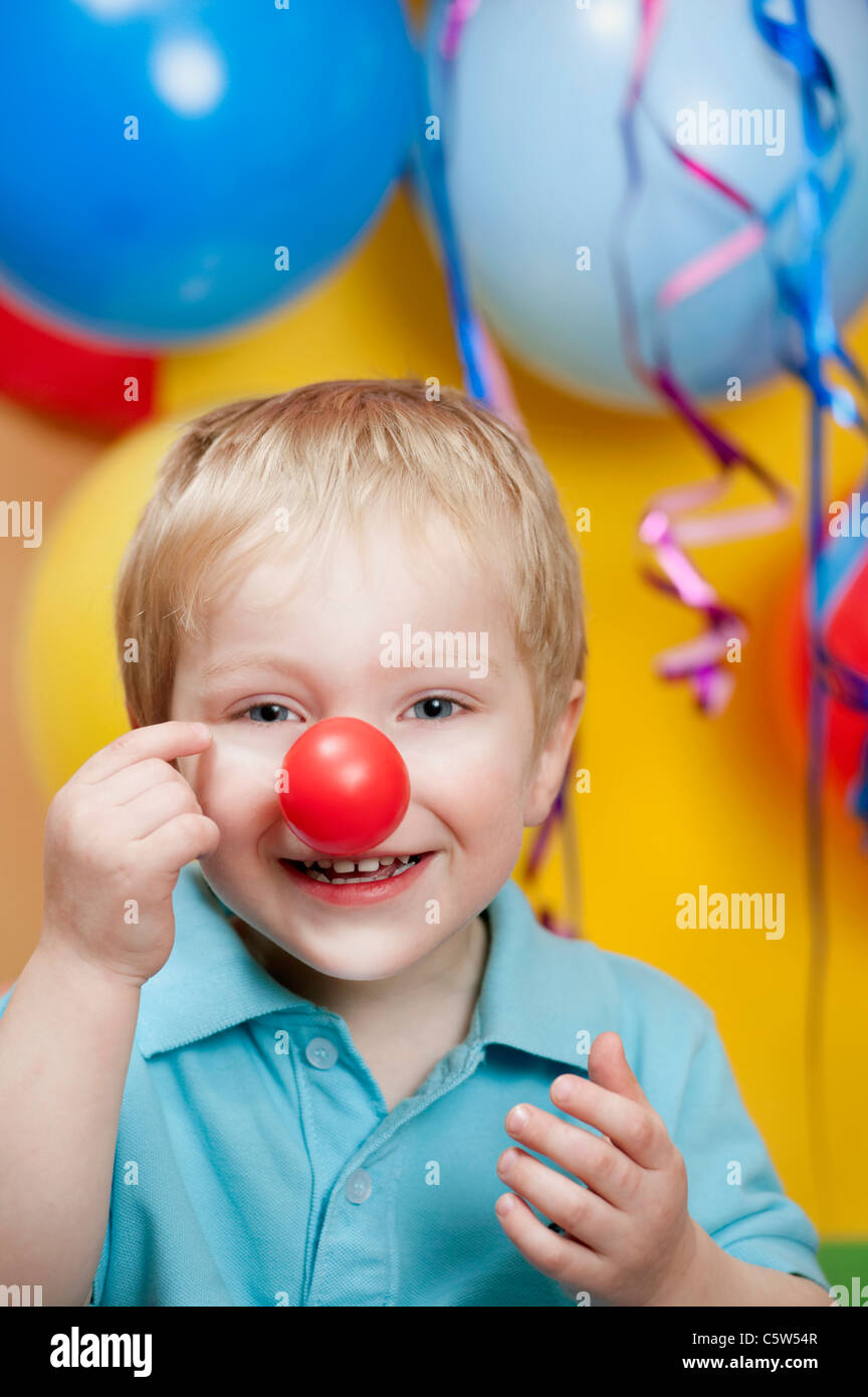 Ragazzo in parte con clown naso e palloncini in background, sorridente, ritratto Foto Stock