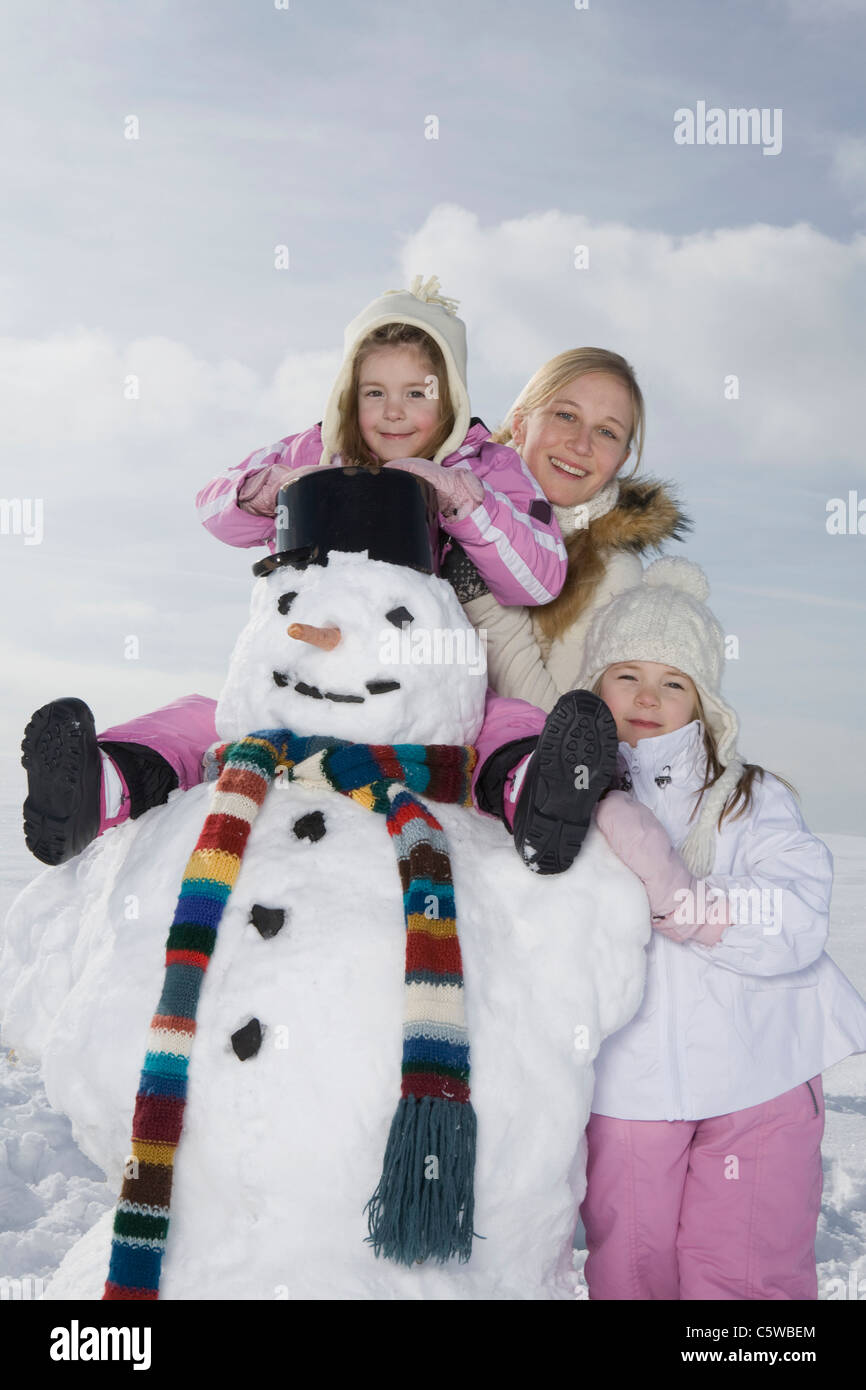 In Germania, in Baviera, Monaco di Baviera, la madre e le figlie (4-5) (8-9) in piedi accanto al pupazzo di neve, sorridente, ritratto Foto Stock