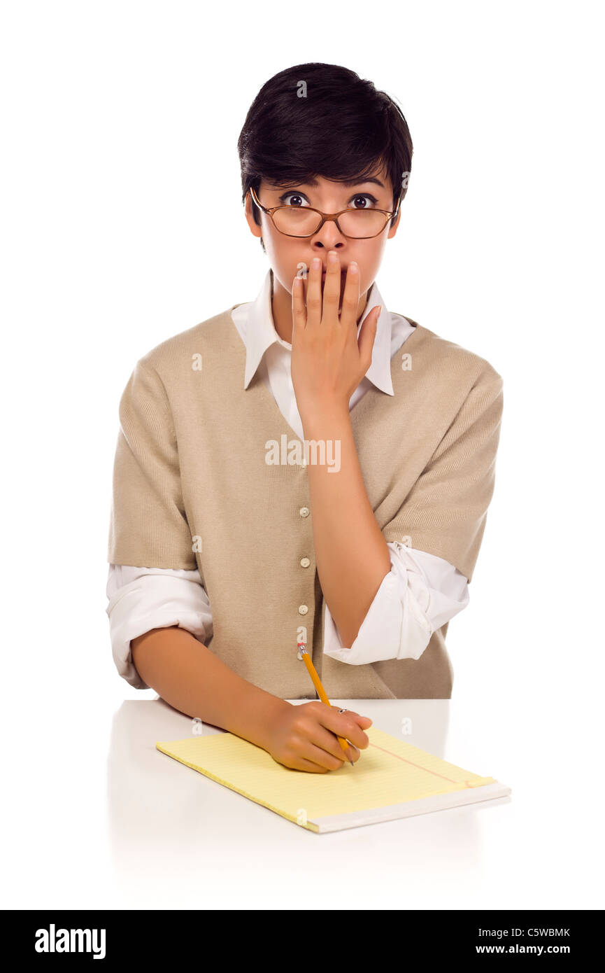 Scioccato razza mista giovane femmina adulta studente a tavola con imbottitura di carta e matita isolato su uno sfondo bianco. Foto Stock