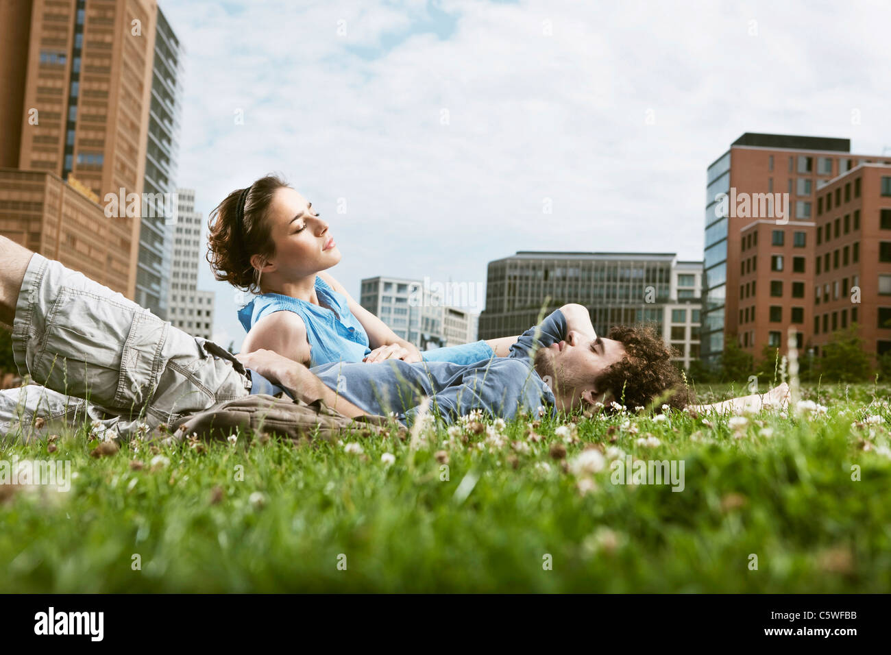 Germania Berlino giovane coppia giacendo in prato, edifici alti in background Foto Stock