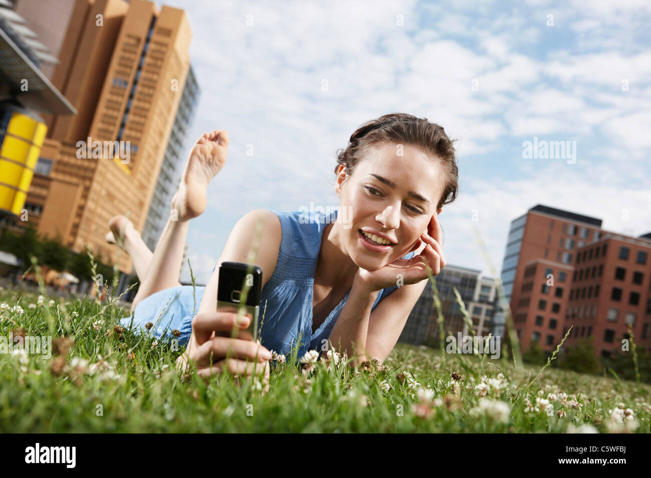 Germania Berlino, giovane donna sdraiata nel prato, utilizzando il telefono cellulare e il ritratto Foto Stock