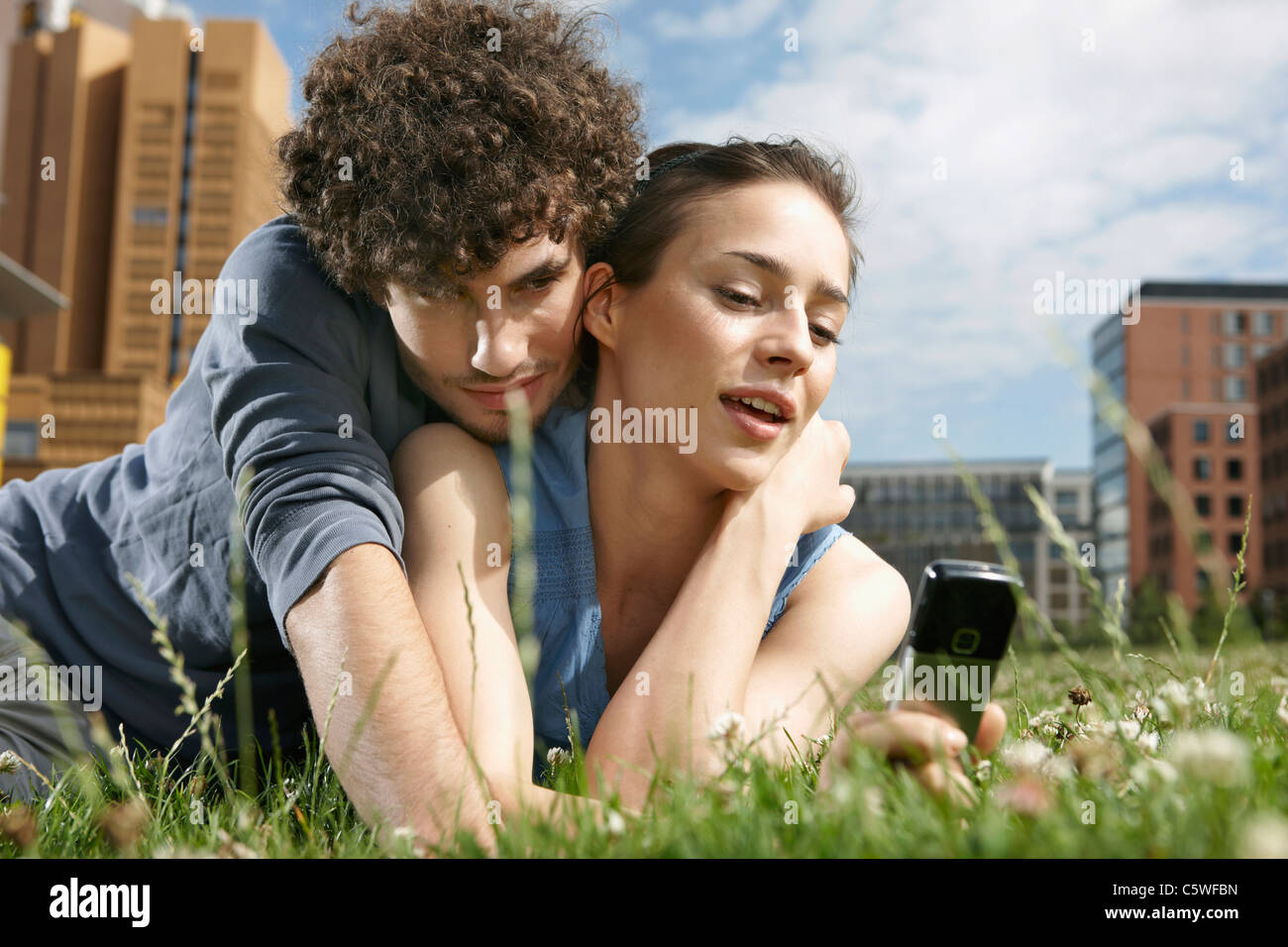 Germania Berlino giovane coppia giacendo in prato, donna tenendo il telefono cellulare, ritratto, close-up Foto Stock