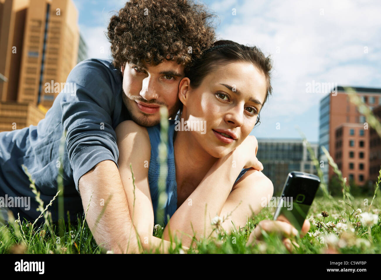 Germania Berlino giovane coppia giacendo in prato, donna tenendo il telefono cellulare, ritratto, close-up Foto Stock