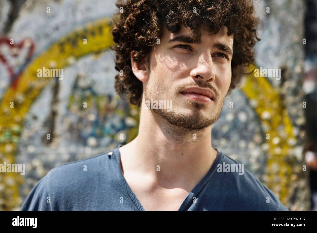 Germania, Berlino, giovane uomo in piedi di fronte a muro con graffiti, ritratto, close-up Foto Stock