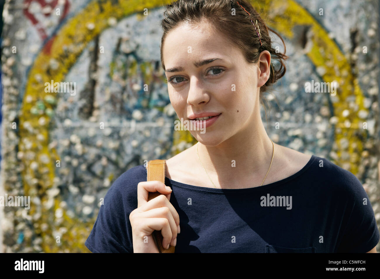 Germania, Berlino, giovane donna in piedi di fronte a muro con graffiti, ritratto, close-up Foto Stock