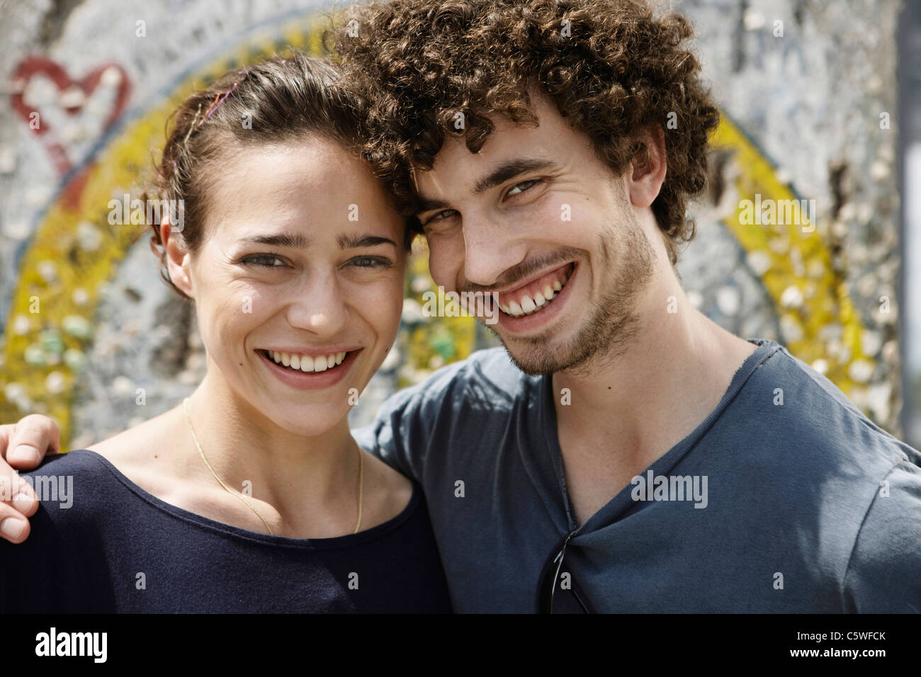 Germania Berlino giovane coppia in piedi di fronte a muro con graffiti, ritratto, close-up Foto Stock