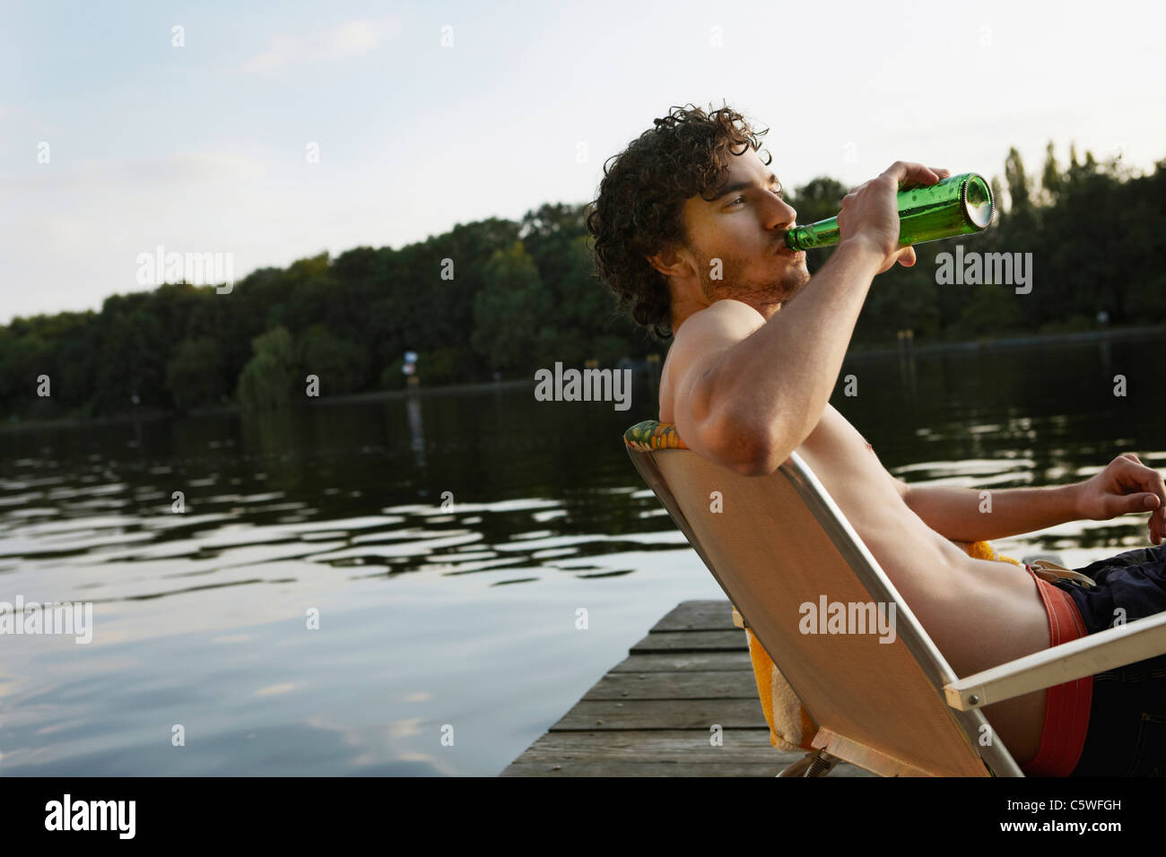 Germania, Berlino, giovane uomo bere bevande in bottiglia, vista laterale, ritratto Foto Stock