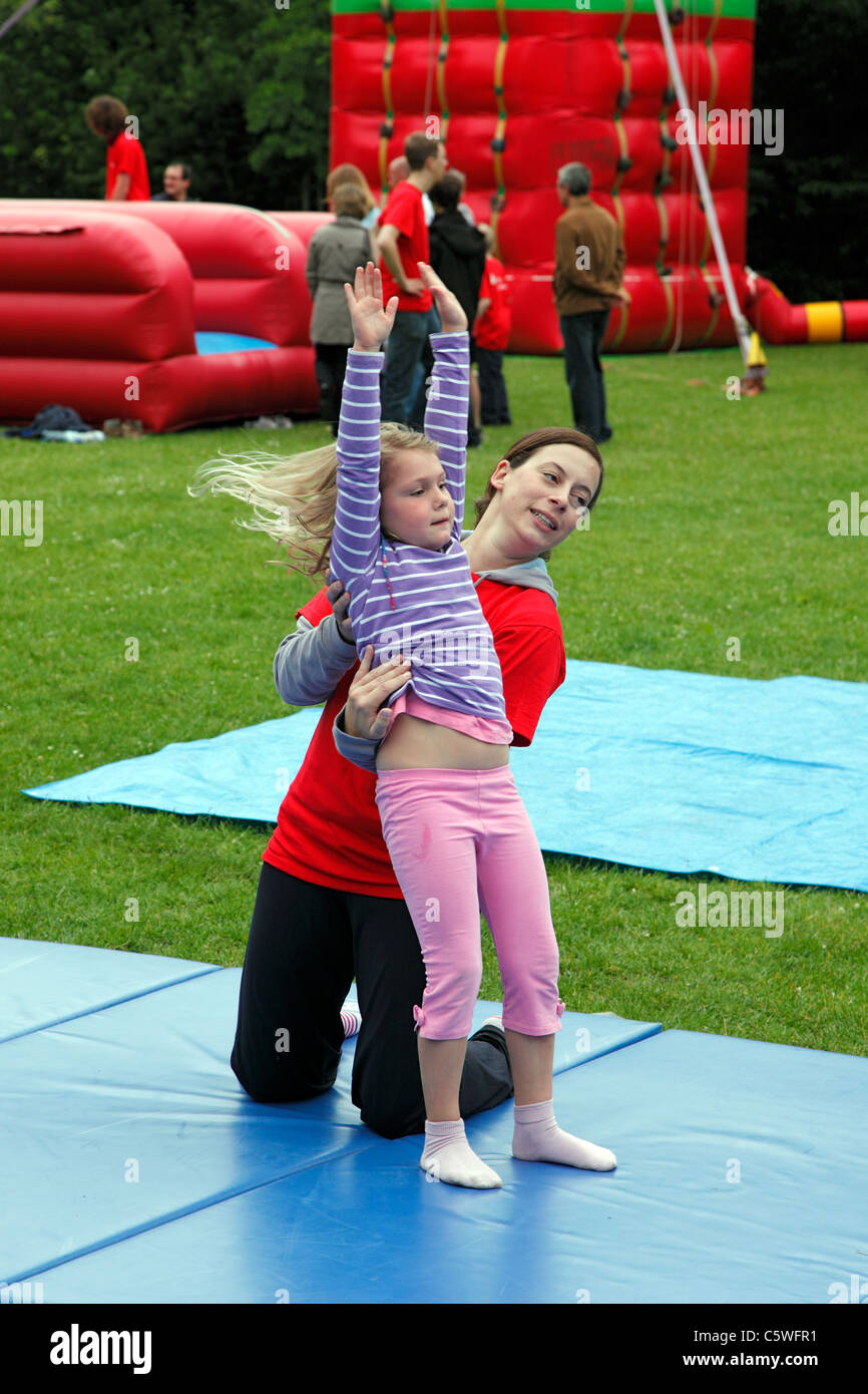 D-Kiel, Kiel Fjord, Mar Baltico, Schleswig-Holstein, Kieler Woche 2011, evento di vela, fiere estive, Hiroshima Parco, giornata di sport, il festival dei bambini, bambini ragazza in un esercizio ginnico, giovane donna aiuta a Foto Stock