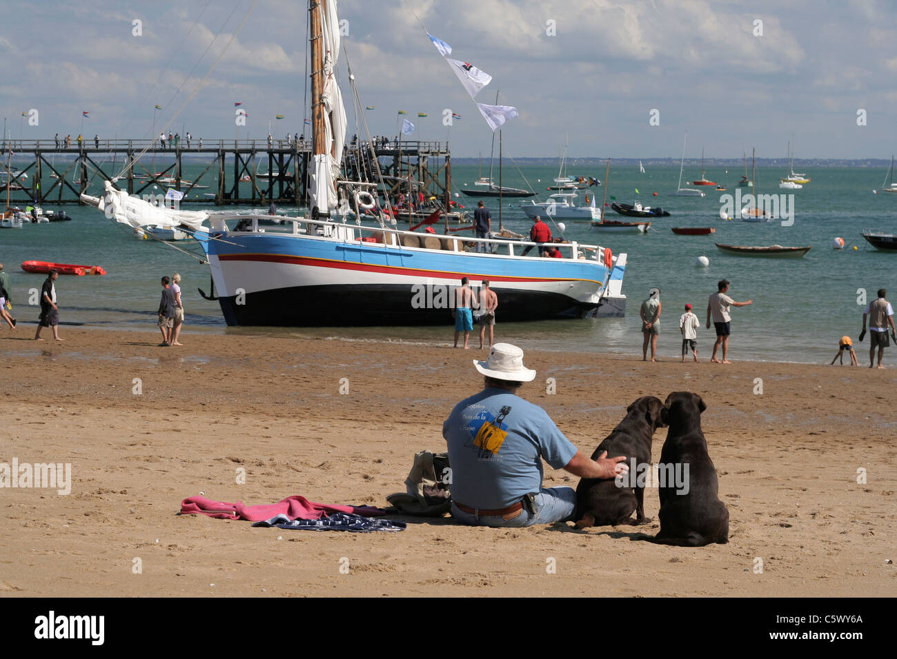 Una barca tradizionale spiaggiata. Un uomo con due cani sulla spiaggia (Plage des Dames,, Noirmoutier Vendée, Francia). Foto Stock