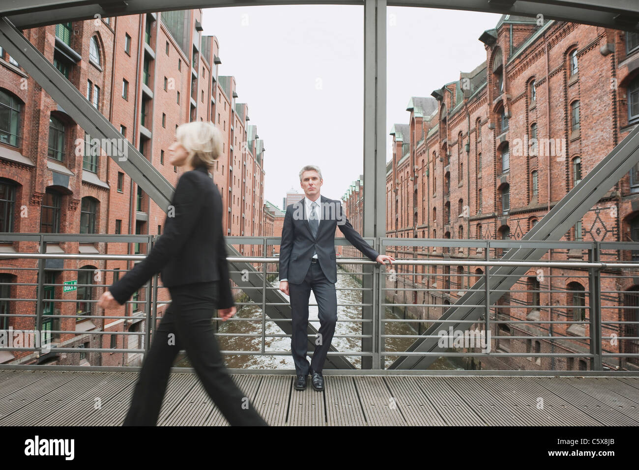 Germania, Amburgo, imprenditrice attraversando il ponte, imprenditore in background appoggiata contro la ringhiera di protezione Foto Stock