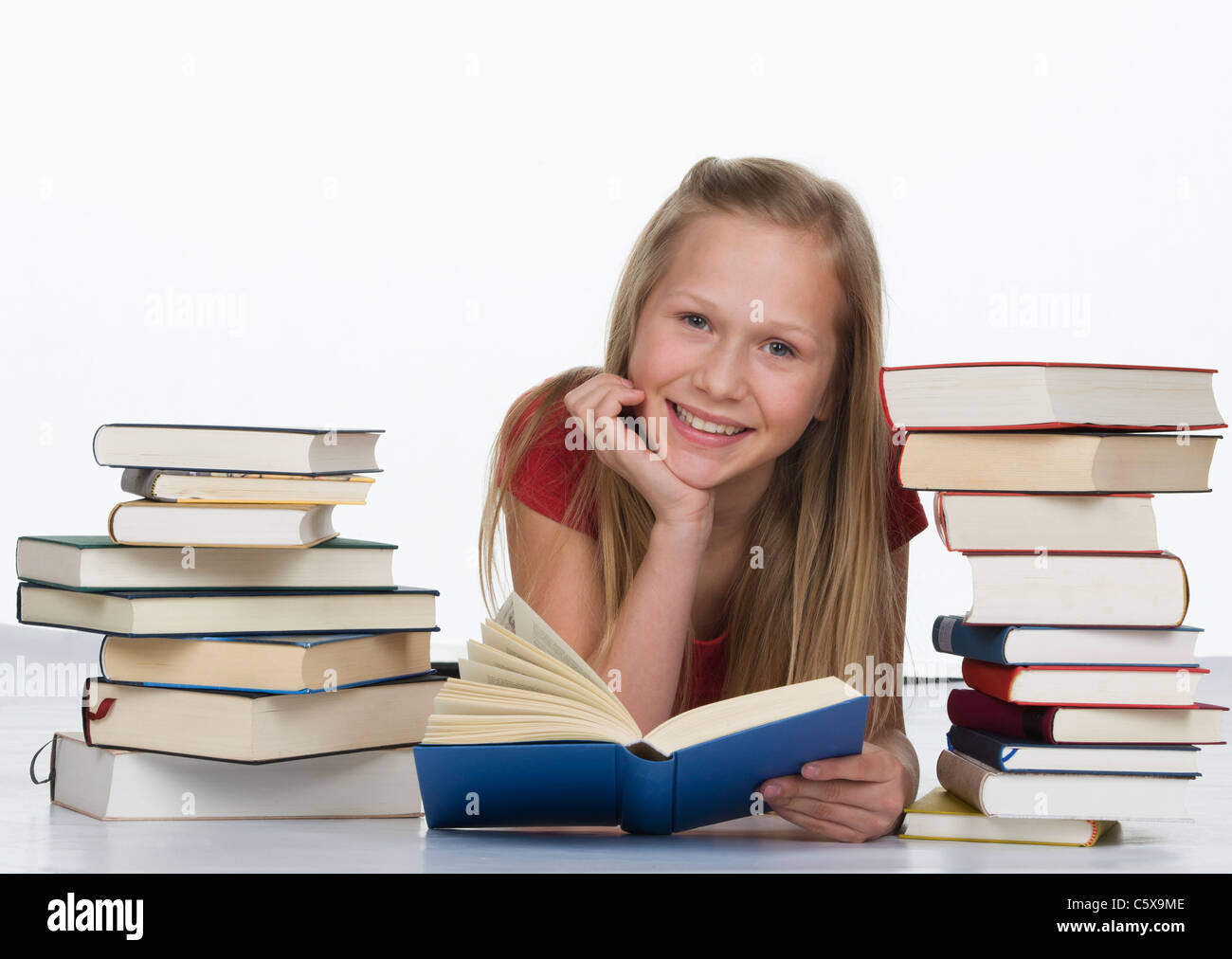 Ragazza con libro oltre a pila di libri contro uno sfondo bianco, sorridente , ritratto Foto Stock