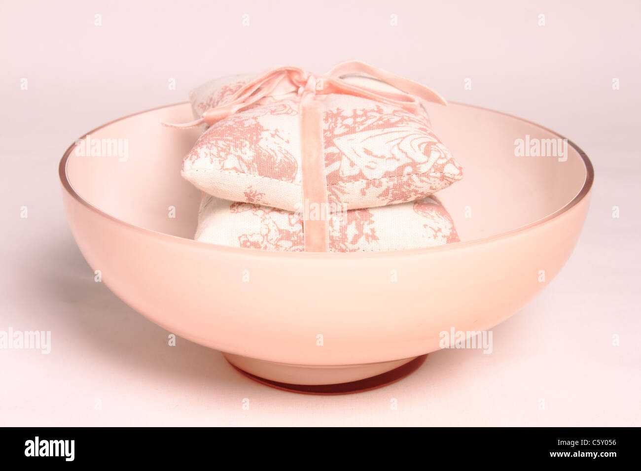 Ciotola rosa rosa con cuscini a motivi geometrici in esso legato con un inchino su sfondo bianco Foto Stock