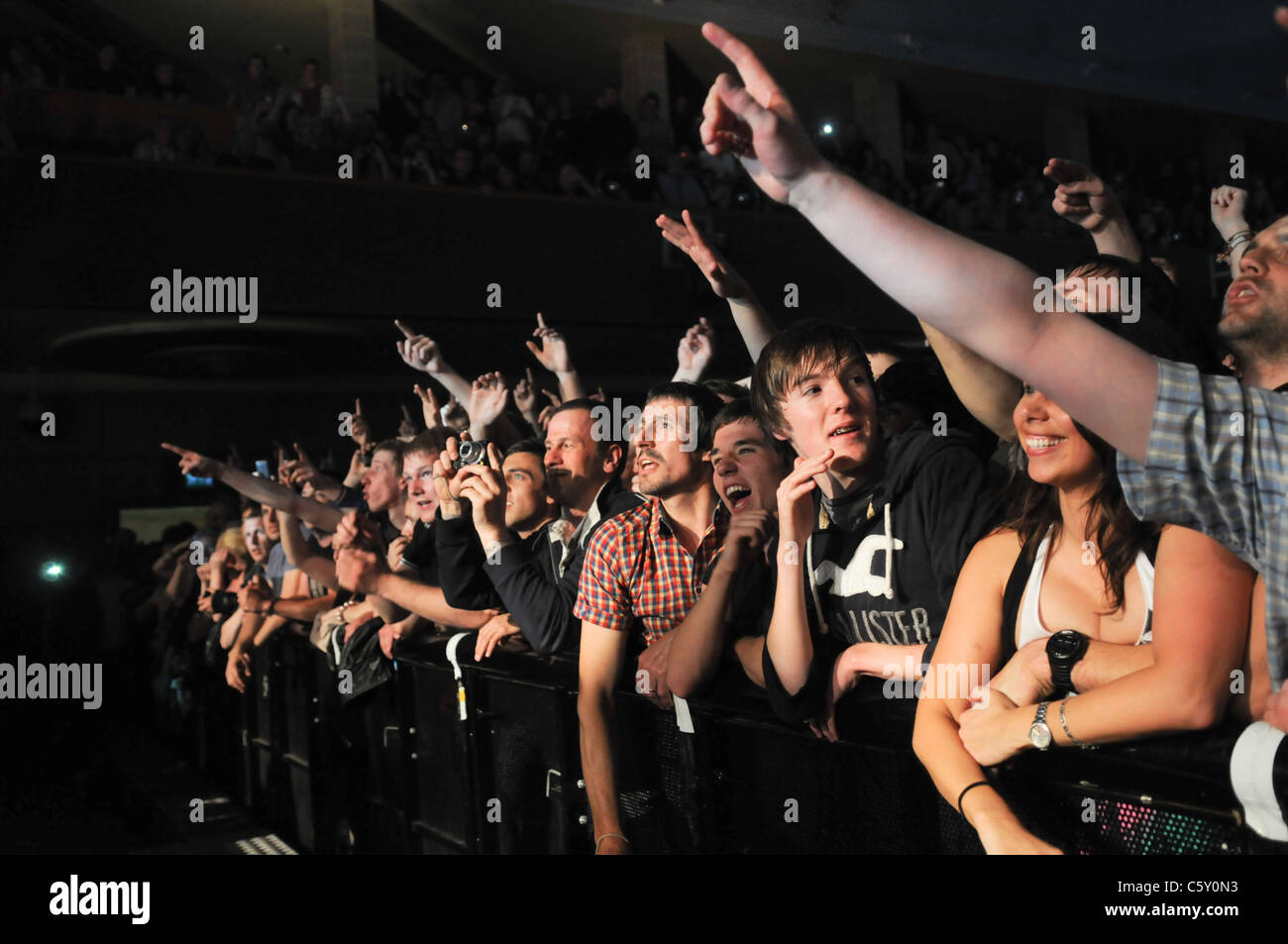 Caldo, sudato giovani tifo folla presso la parte anteriore di un concerto di musica premendo contro una barriera urlando in una band dal vivo sul palco Foto Stock