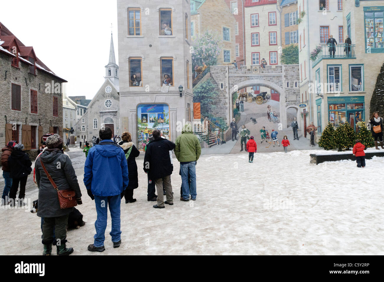 Quebecois Life Mural Old Town Quebec City Canada // QUEBEC CITY, Canada - Un enorme murale sul lato di un edificio nella città vecchia di Quebec City raffigura e idilliaca vita Quebecois. I turisti si trovano sul terreno innevato che guarda il murale. Foto Stock