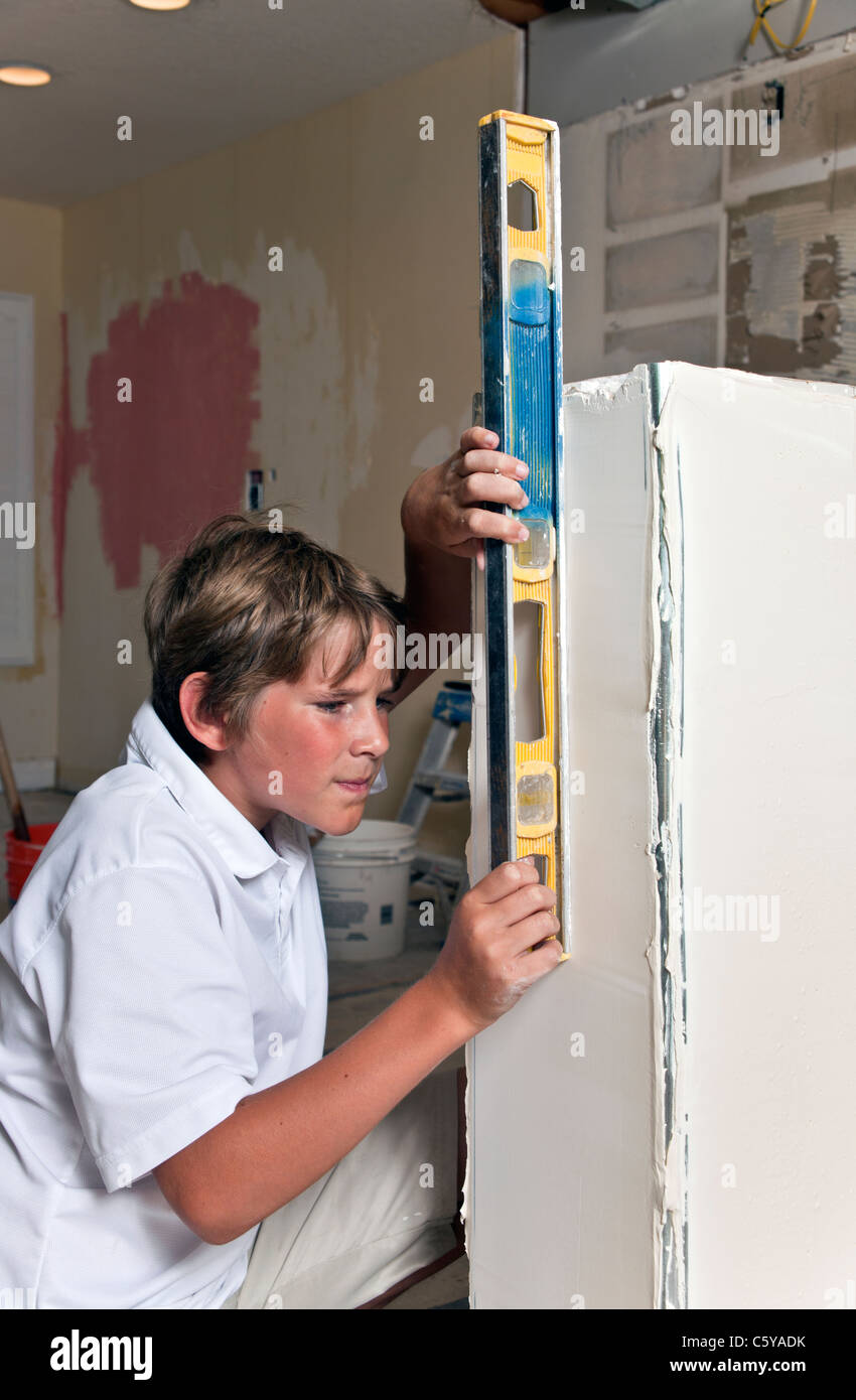 Esperienza di lavoro aiutando 11-12 anni vecchio ragazzo caucasico strumento controlla il livello verticale di parete pony durante il rimodellamento della cucina. Signor © Myrleen Pearson Foto Stock